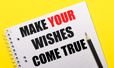 White notebook with inscription MAKE YOUR WISHES COME TRUE written in black pencil on a bright yellow background.