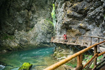 Young female photographer in colourful jacket hiking a trail along a clear river through the Vintgar Gorge in Slovenia
