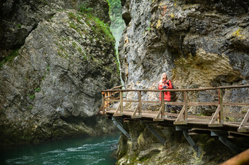 Young female photographer in colourful jacket hiking a trail along a clear river through the...