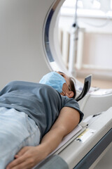 A woman in a medical mask lies on the tomograph table. woman is undergoing computed axial...