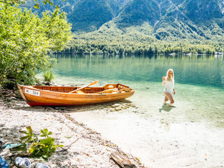 Blonde woman standing in the Bohinj Lake, next to a boat on the beach