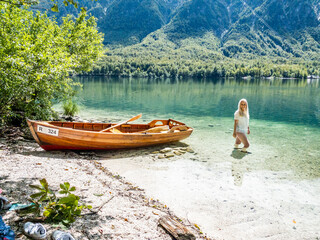 Blonde woman standing in the Bohinj Lake, next to a boat on the beach