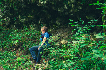 male photographer sitting in the green forest under a rock wall