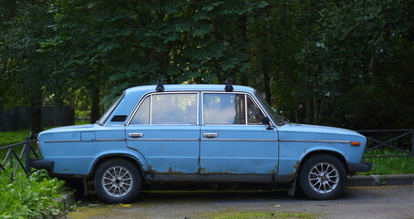 Fototapeta premium An old blue Soviet car in the courtyard of a residential building, Dybenko Street, St. Petersburg, Russia, July 2021