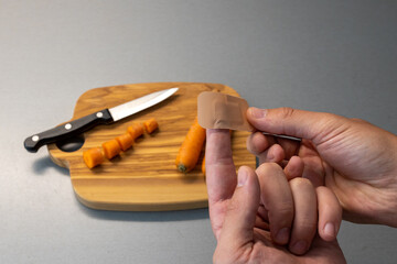 Close-up of a wound patch on a finger. cut into the finger while cooking. Care bloody wound at home. in the background is a cutting board, a knife and carrots. 