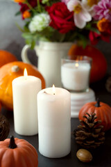 Autumn creative background with candles, autumn flowers, pine cones and pumpkins. Dark moody, cozy fall