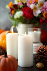 Autumn creative background with candles, autumn flowers, pine cones and pumpkins. Dark moody, cozy fall