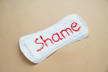 Woman's sanitary pad with word shame. Abstract social concept of shaming women for their menstrual...