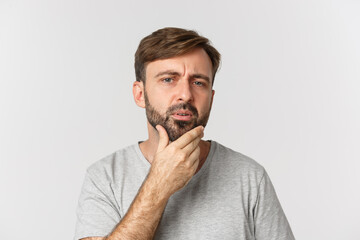 Close-up of confused man touching his beard and looking at himself, need to shave, standing over...