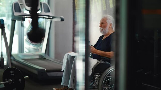 Disability retired old man drinks water and rests in the gym.