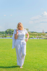 Fototapeta na wymiar Blonde woman of plus size, American or European appearance walks at golf field, enjoying life. Young lady with excess weight, stylishly dressed at white .Natural beauty