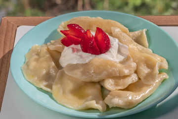 Dumplings stuffed with cottage cheese. With dressing of thick, fatty sour cream. On plate of turquoise color, decorated with strawberries. Topic - hot dish, homemade food, dough products