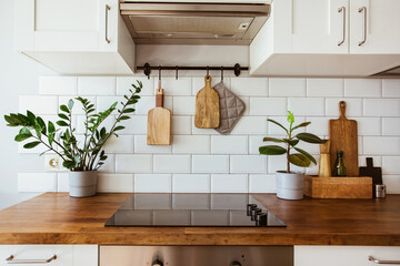Kitchen brass utensils, chef accessories. Hanging kitchen with white tiles wall and wood tabletop.Green plant on kitchen background - obrazy, fototapety, plakaty