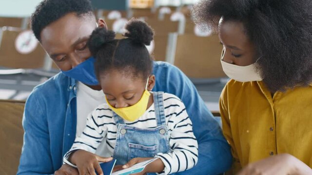 Cute multiracial little girl sitting in the airport with her parents and they looking at their passports, while waiting at their departure