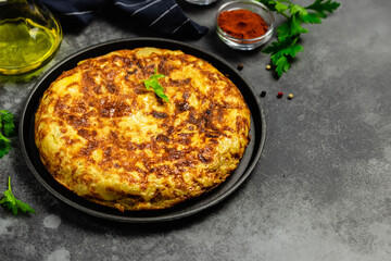 Authentic Spanish tortilla in cast iron skillet, dark background. Space for text.