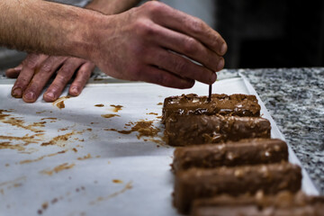 Hands of white male pastry chef hands of haute cuisine cake design, dipping chocolate cakes by hand. Close up view
