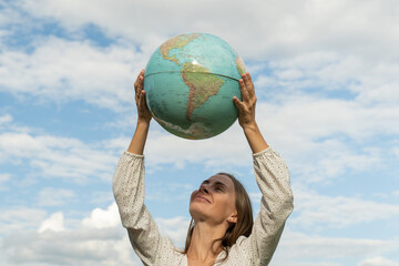 The concept of sustainable ecology and the global environment with a woman holding a globe over her head against the blue sky