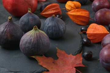 Selective focus to group of fresh ripened purple figs on blurred black background with autumn red orange leaves. Colorful seasonal texture with fall mood.