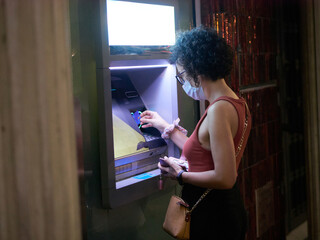 A young woman withdraws money from an ATM machine at night