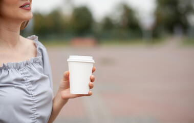 White paper cup with coffee in woman hand. Time for drink coffee in city. Coffee to go. Enjoy moment, take a break. Disposable paper cup closeup. Delicious hot beverage. Blank space for text, mockup