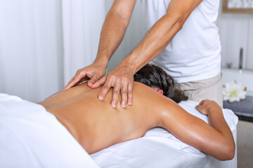 Relaxed young woman lying face down on massage table and enjoying remedial body massage by...