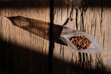 Roasted Coffee Beans From Plastic Bag Packaging On Wood background Color Retro style.Selective Focus only coffee beans. Highlight and shadow with copy space for text layout.