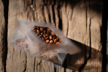 Roasted Coffee Beans From Plastic Bag Packaging On Wood background Color Retro style.Selective Focus only coffee beans. Highlight and shadow with copy space for text layout.