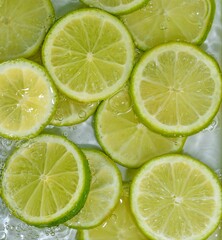 Close-up fresh slices of green limes on white background. Slices of limes in sparkling water on white background, closeup. Citrus soda