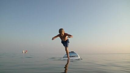 Happy child enjoying time in vacation on sea beach. Boy funny jumping to water from board on travel holiday at sunset.