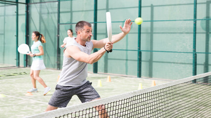 Obraz premium Man training to play tennis on the padel court outdoor. Athletes training in the background