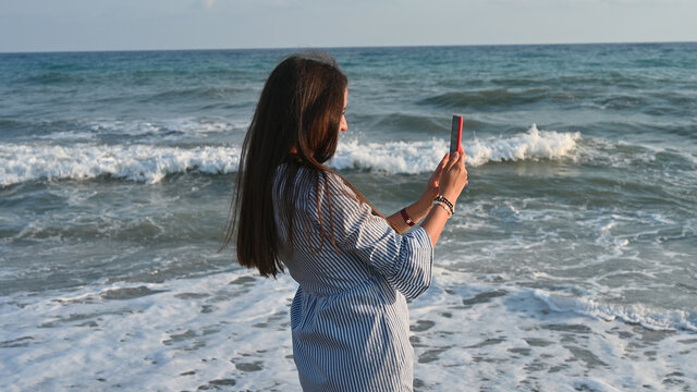 Young woman taking pictures of the sea as a keepsake