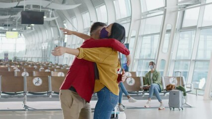 Mixed race young attractive woman walking in terminal lobby with suitcase, and greeting her best friend. Asian woman meeting her male friend at airport. Tight hugs meeting of two people