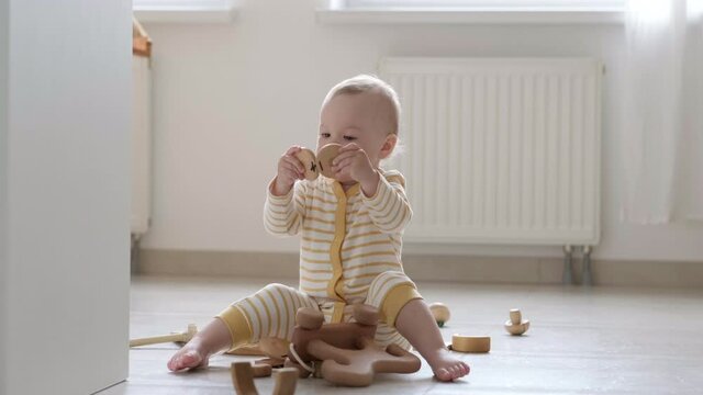 eco wood toy baby game. Little clever caucasian child playing natural toys on floor at home. Educational games for early development. Little kid puts toy in his mouth.