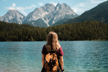 Young blonde woman stops to contemplate Blindsee lake with the Biberwierer Scharte in the background, alpine image in Austria, hiking and happiness in the alps. Backpacking and hiking in nature.