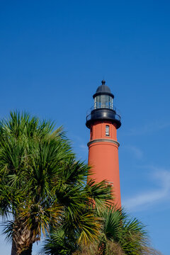 Vertical image of the tallest lighthouse in Florida and second tallest in the United States surrounded by palm trees in late afternoon light