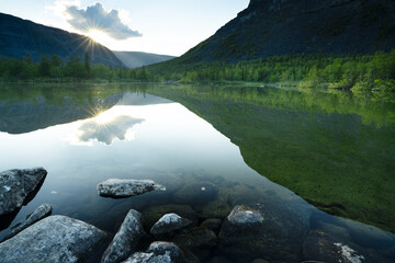 Green mountain lake at sunset with sun reflection