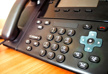 The black desktop push-button telephone. IP phone on desk in office.
