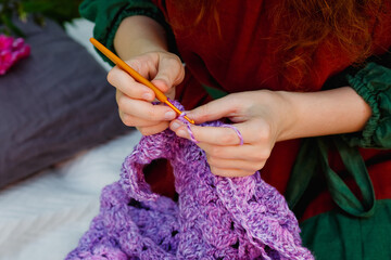 Selective focus. Close-up crochet. Women's hands are knitting a lilac openwork shawl.