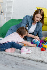 toddler kid with down syndrome playing with smiling kindergarten teacher on carpet