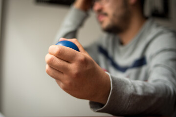 Stressed man with glasses , squeezing little blue stress ball and scratching his head