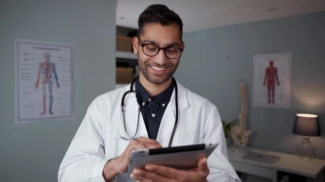 Mixed race male doctor typing on digital tablet standing in doctors office