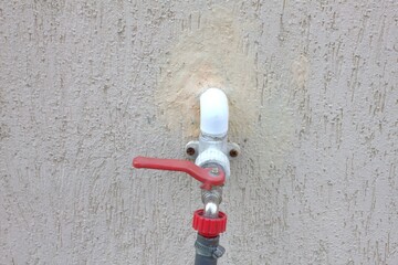 
A ball valve with a red handle and a hose is installed in the wall of the house