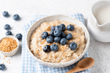 Vegan oatmeal porridge with blueberries and flax seeds in bowl on grey concrete background. Clean eating, dieting, weight loss concept