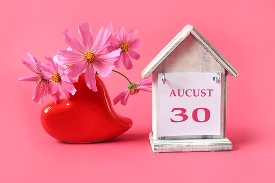 Calendar for August 30 : the name of the month of August in English, the number 30, a cup of tea, books, a bouquet of pink flowers, eyeglasses, an alarm clock on a pink background