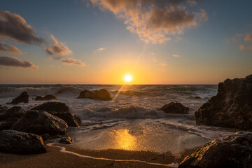 Fototapeta premium A beautiful golden sunset with reflections on the waves washing over the beach and the sun setting behind the horizon.