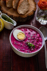 Cold borsch, summer beet soup with fresh cucumber boiled egg in a white bowl, bread, lemon. Traditional European food, delicious lunch