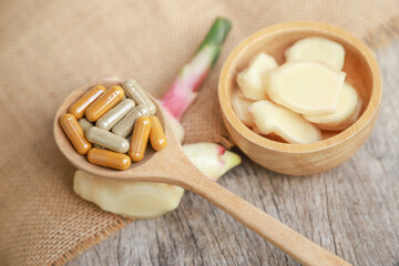 Herbal supplement in capsules with young ginger on wooden table for healthy medicine living