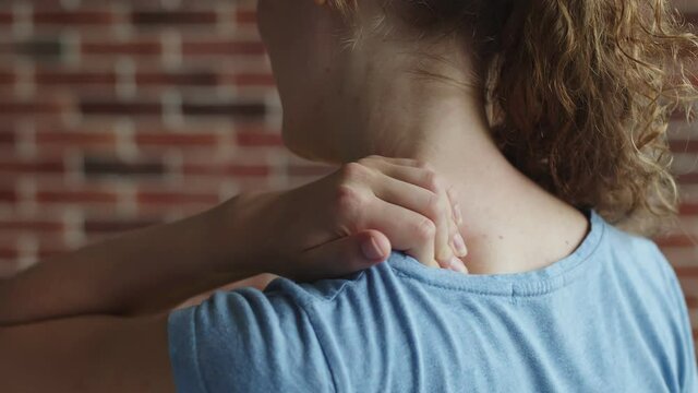 White woman kneads her neck, which hurts, back view, closeup. Red-haired woman is experiencing pain in her neck. Concept of neck pain