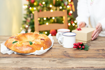 Roscón de Reyes on wooden table with Christmas tree in the background. Christmas lunch.