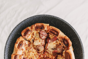 Homemade pizza with sausages and pineapple in a pan.